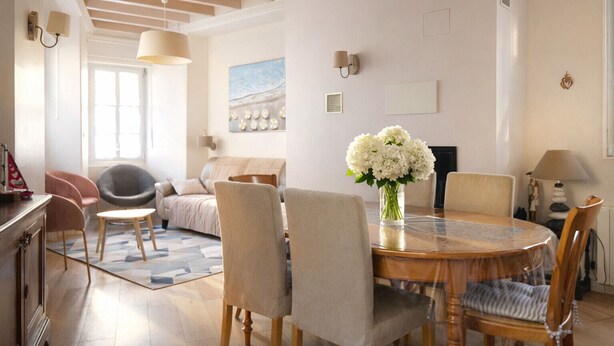 Ein modernes Wohnzimmer mit einem runden Holztisch, beigen Sofas und einer Vase mit weißen Blumen.