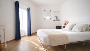 Ein Schlafzimmer mit einem Bett, einem Fenster mit Vorhängen, einem Heizkörper, einer Tür mit Wappen und einem Bild an der Wand.