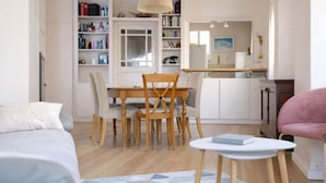 Ein modernes Wohnzimmer mit Essbereich, einer Küche im Hintergrund und einem Bücherregal voller Bücher.