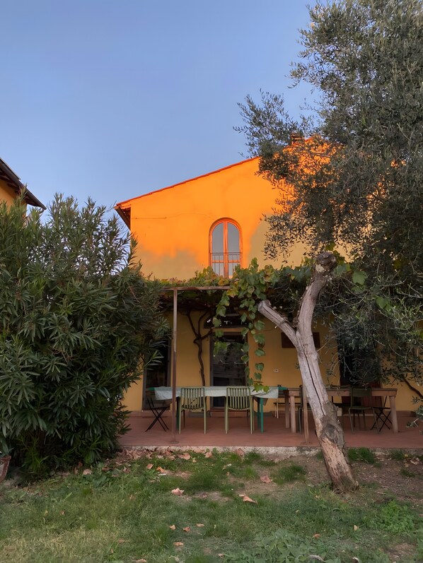 A building with a yellow facade, a window, and a covered outdoor seating area with tables and chairs.