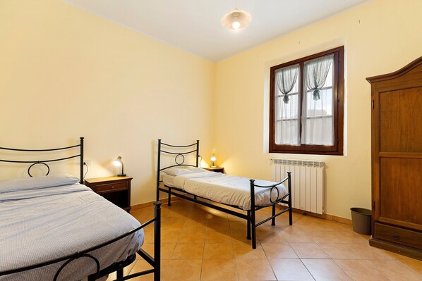 Une chambre à coucher avec deux lits en métal, une armoire en bois, un radiateur et une fenêtre avec des rideaux.
