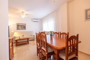 Un comedor con una mesa y sillas de madera, un sofá blanco, una lámpara de pie y un ventilador de techo.