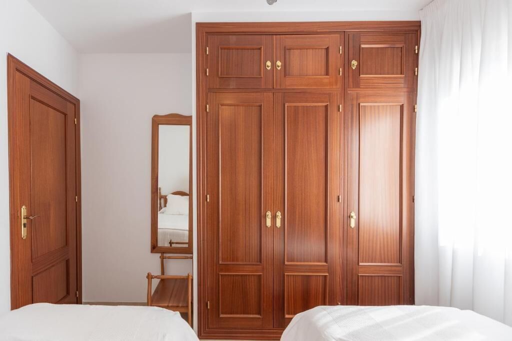 A bedroom with two beds, a wooden wardrobe, and a mirror.
