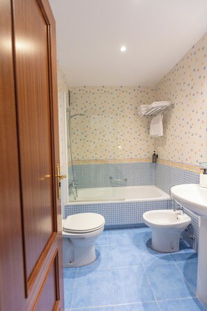 A bathroom with a bathtub, two toilets, a sink, and a shower. - Apartamentos Miguel Ángel  (Estepona)