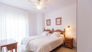 Un dormitorio con dos camas, una mesita de noche de madera, una mesa y un ventilador de techo.