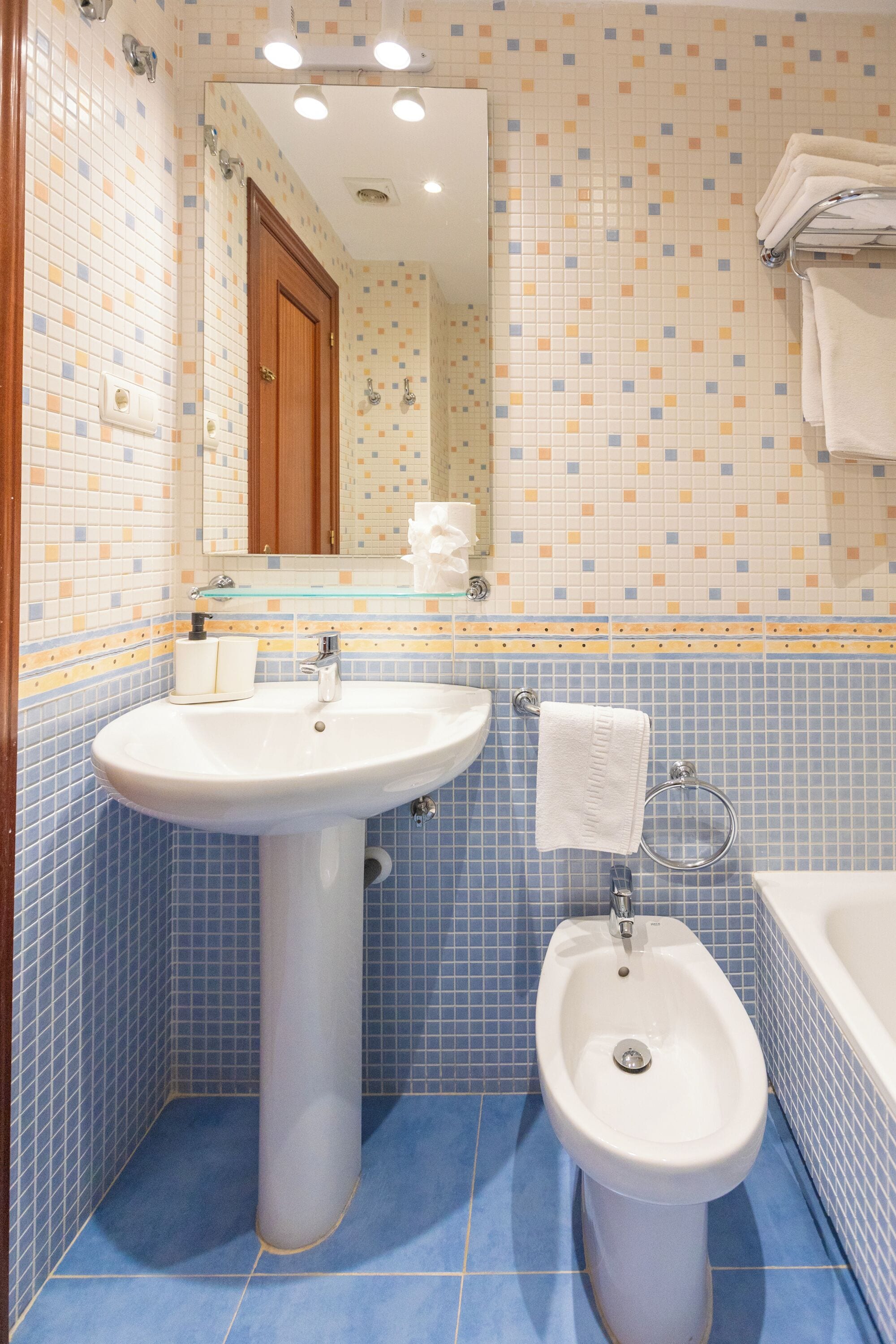 Un baño con lavamanos, bidé y bañera blancos, con azulejos en azul y beige.