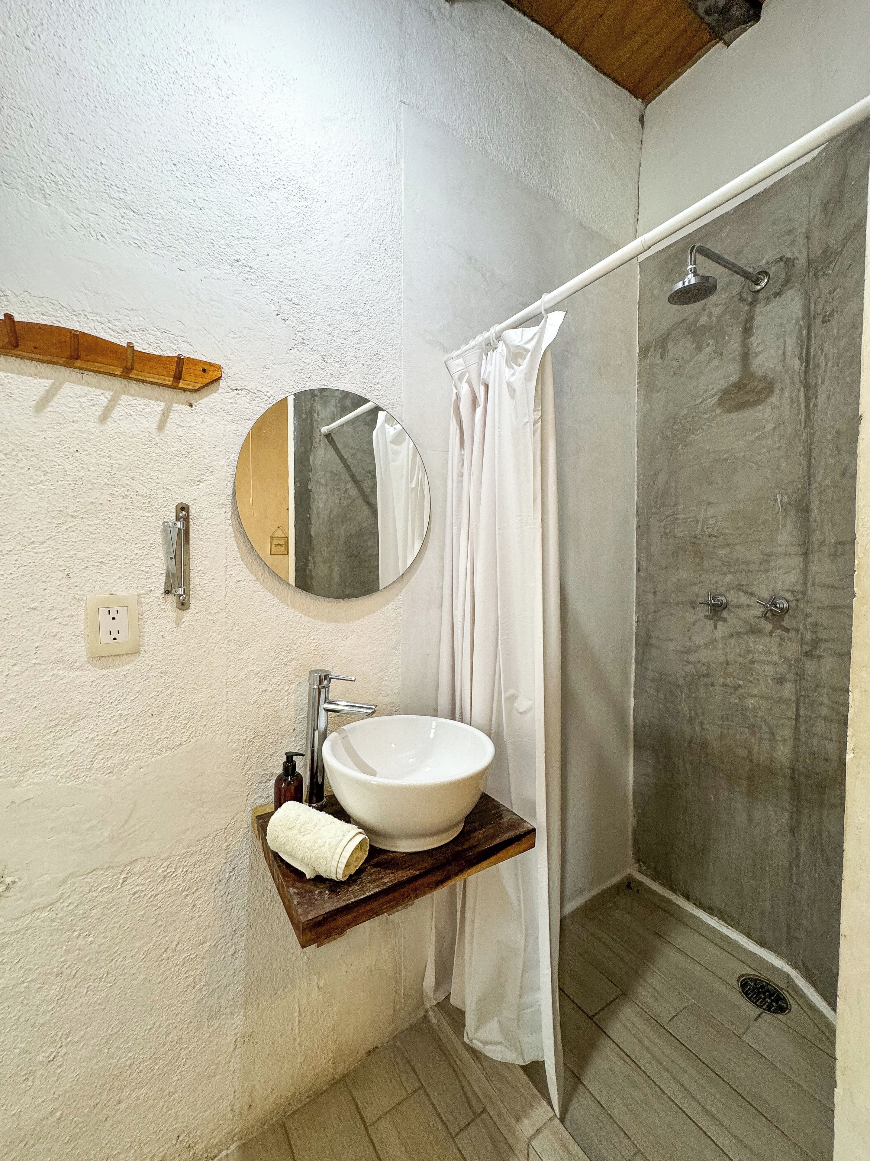 Un baño con un espejo redondo, un lavabo blanco y una zona de ducha.