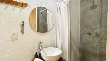 Un baño con un espejo redondo, un lavabo blanco y una zona de ducha.