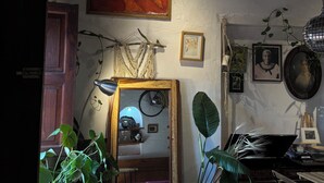 A rustic room with a wooden door, a mirror reflecting a bicycle, and various framed artworks on the wall. - Hostal Casa de Zeferina (Tuxtla Gutiérrez)