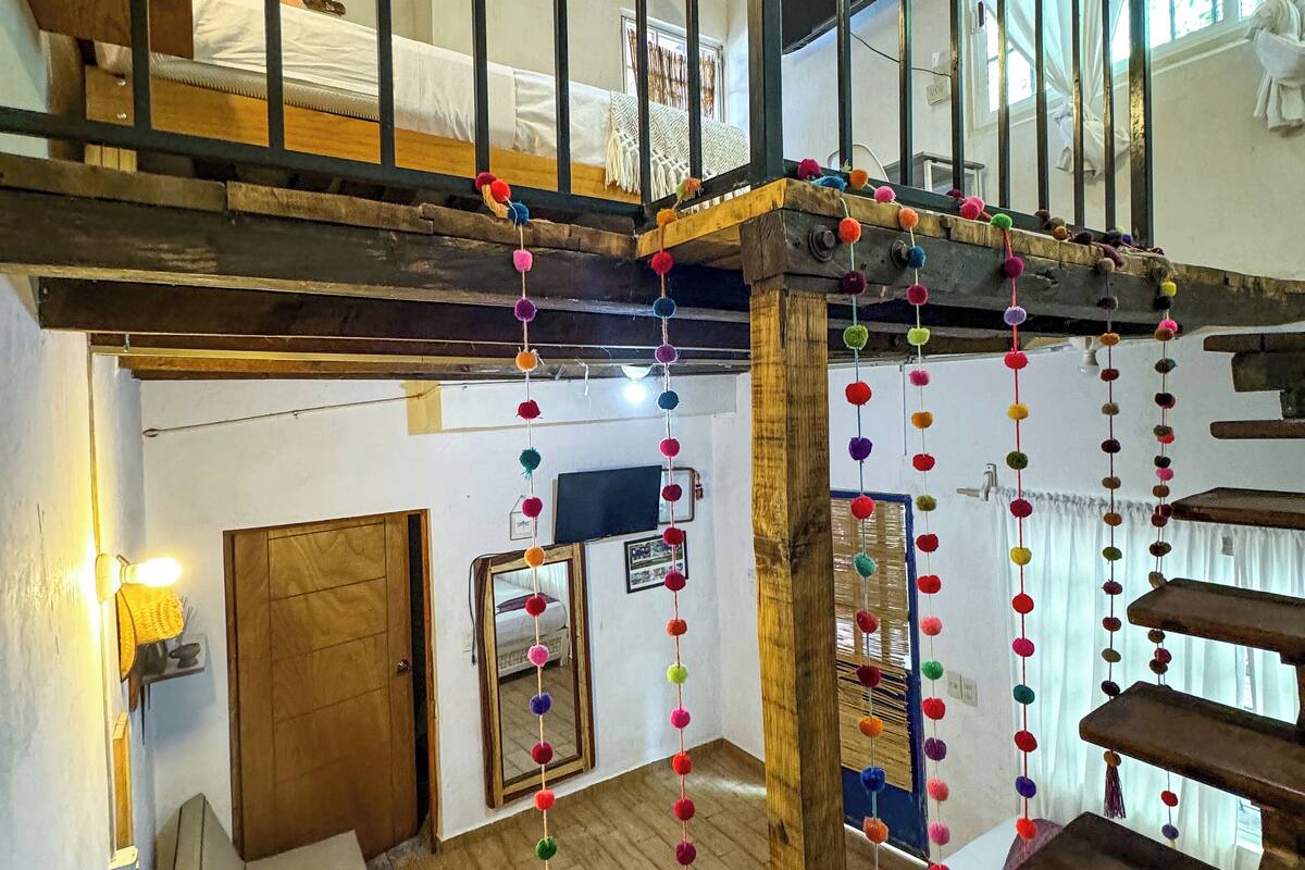 Une pièce à plusieurs niveaux avec un escalier en bois, un lit en mezzanine et une décoration suspendue.