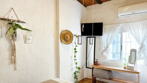 A cozy room with a bed, a wooden table, a hanging plant, a wall-mounted TV, and an air conditioning unit. - Hostal Casa de Zeferina (Tuxtla Gutiérrez)