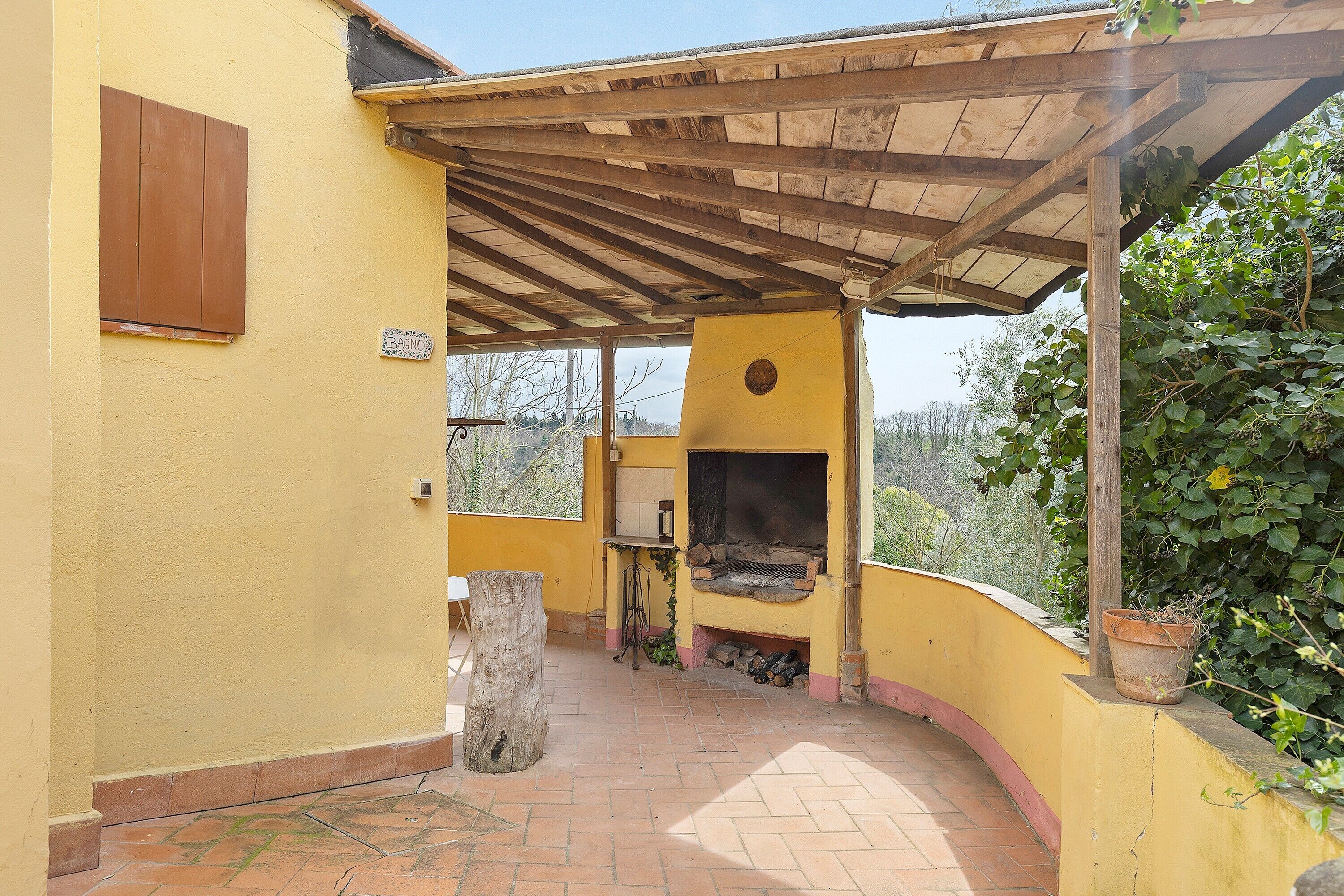 A covered outdoor area with a wooden pergola, a brick floor, and a yellow wall.