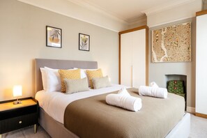 Une chambre d’hôtel avec un grand lit, une table de chevet avec une lampe, deux œuvres d’art encadrées au mur et une carte décorative au-dessus du lit.