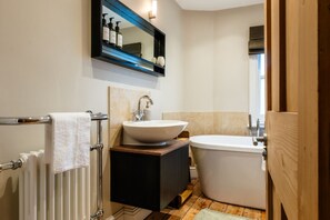 A bathroom with a white sink, a freestanding bathtub, a mirror with toiletries, and a radiator. - Stunning 2 Bed Townhouse with Patio in Cheltenham (Cheltenham)