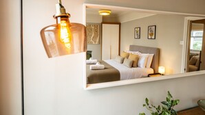 Ein Schlafzimmer mit Bett, Kissen, Nachttisch, Lampe und Spiegel.