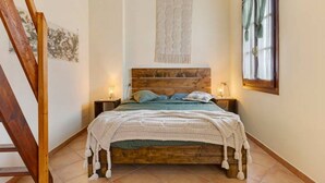 Un dormitorio con una cama de madera, un tapiz colgante, una ventana con cortinas y una escalera.