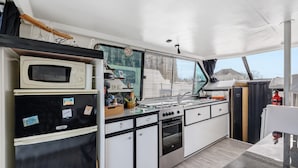 A compact kitchen with a microwave, stove, oven, and a window with blinds.