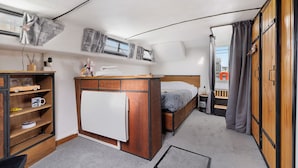 A compact bedroom with a bed, a small desk, a wardrobe, and a window with curtains.