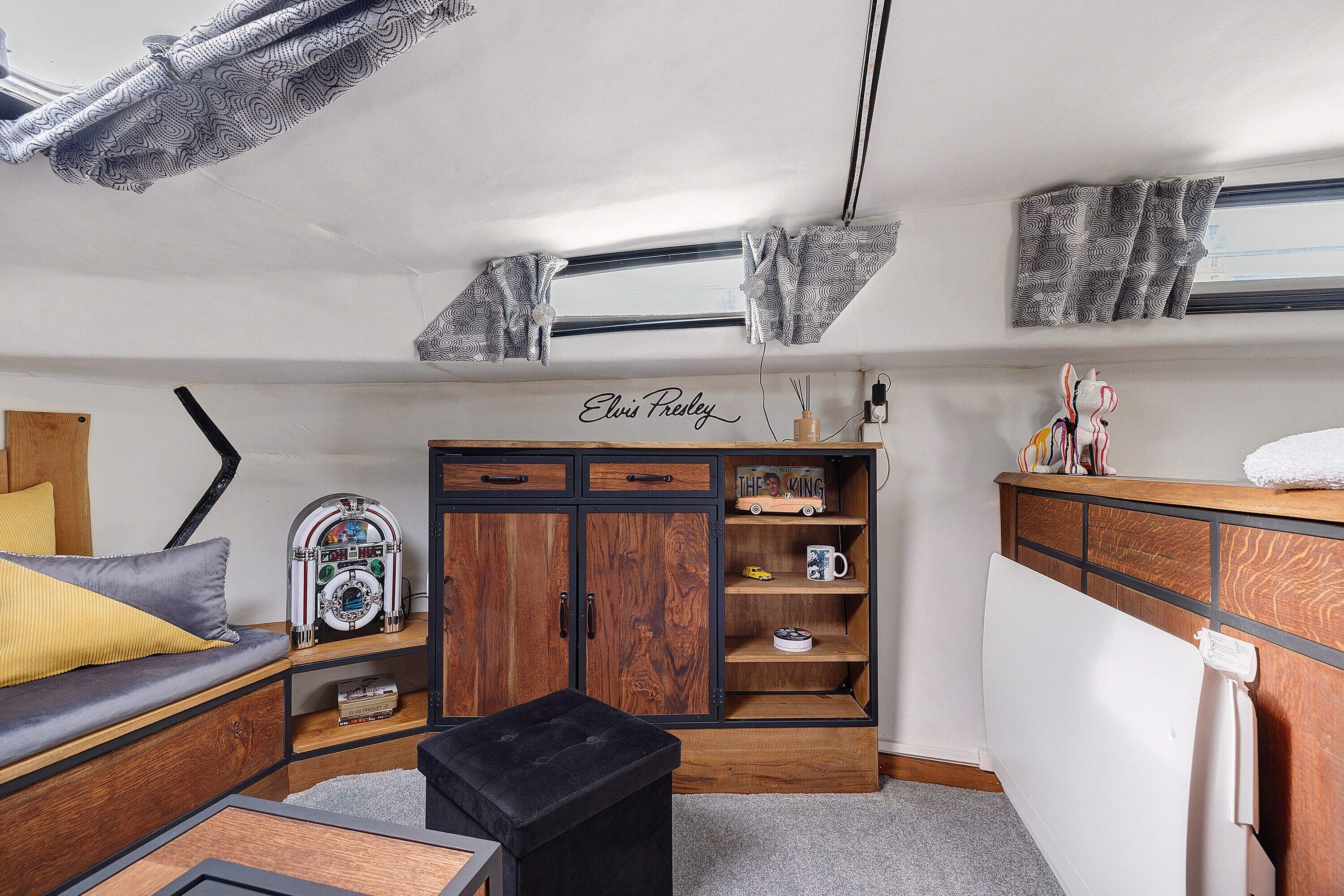 A compact living space with a sofa, a small table, a cabinet with shelves, and a radiator.