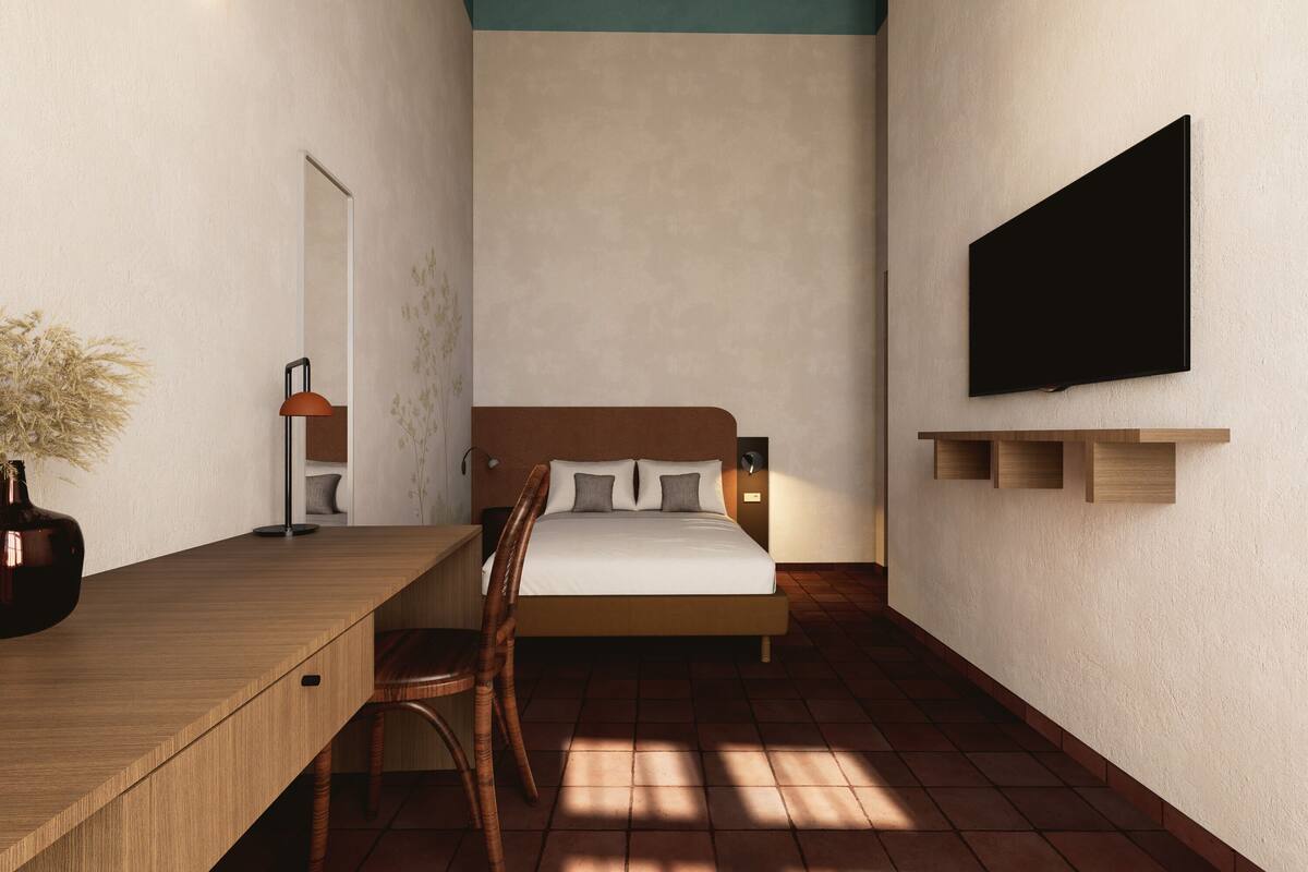 A bedroom with a bed, a desk, a chair, a TV, and a wall-mounted shelf.