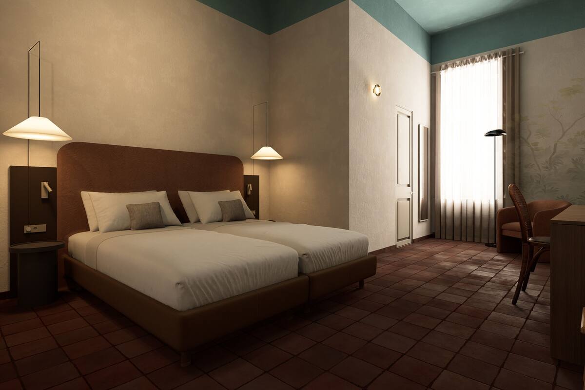A double bed with two bedside tables, a chair, and a desk in a room with tiled flooring and a blue accent wall.