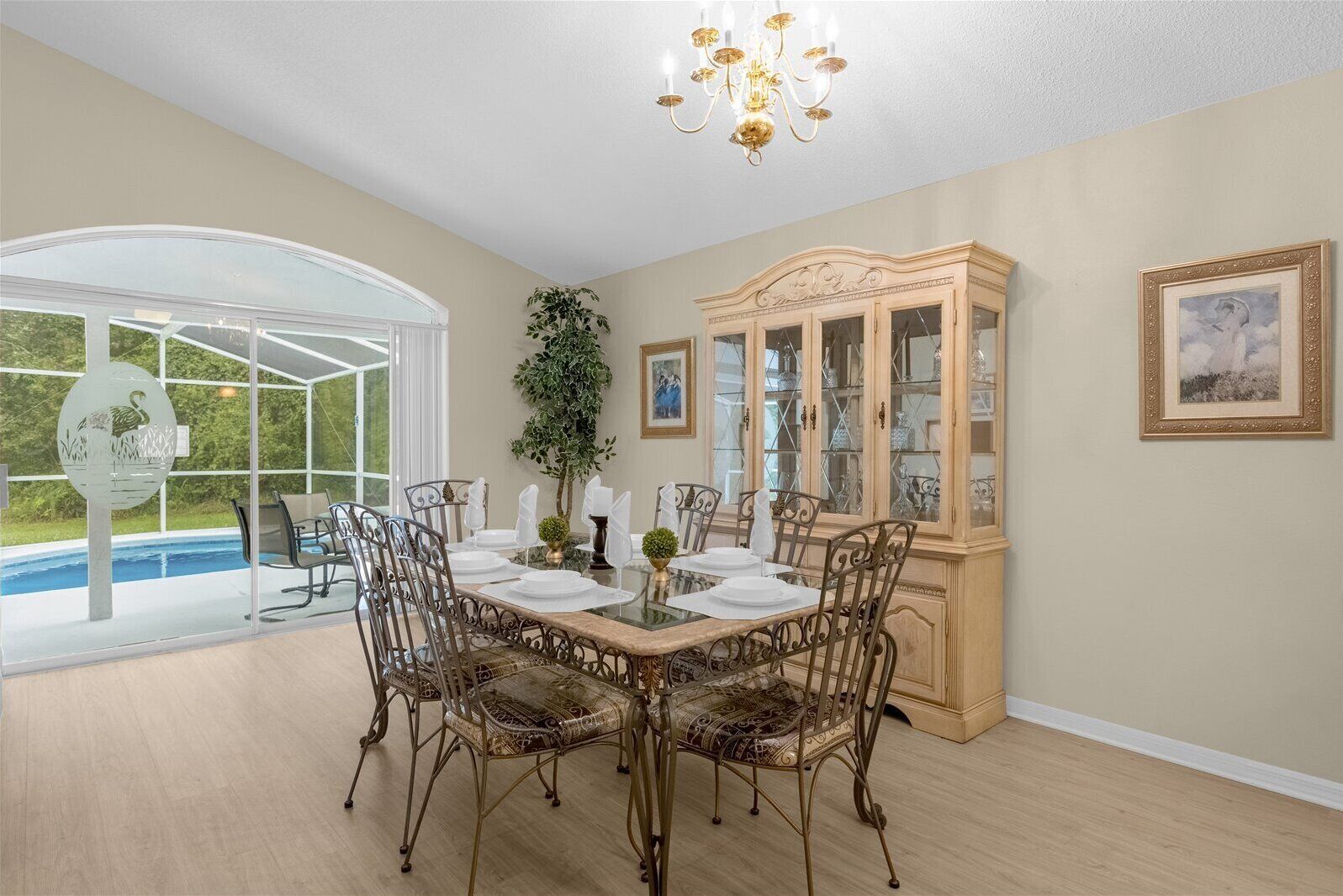 Un coin repas avec une table en verre, des chaises en métal, un buffet en bois et une vue sur une piscine.