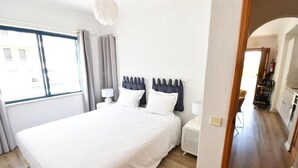 Un dormitorio con una cama grande, una mesita de noche, una lámpara y una ventana con cortinas.