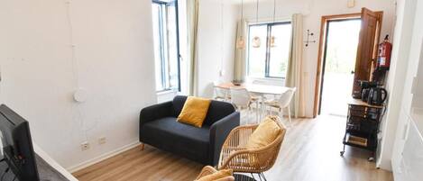 A modern living room with a sofa, chairs, a dining table, and a kitchen area with a coffee machine.