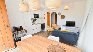 Una habitación de hotel compacta con una mesa de comedor de madera, televisión, kitchenette y mobiliario de mimbre.
