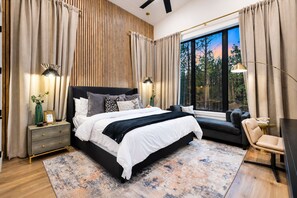 A modern bedroom with a large bed, bedside tables, a seating area, and a view of the outdoors. - Luxe & Kid Approved! Playset, EV, Meta VR Game (Broken Bow)
