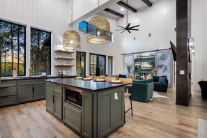 A modern kitchen with a central island, large windows, and a ceiling fan. - Luxe & Kid Friendly | VR, Playset & 2 King Suites (Broken Bow)