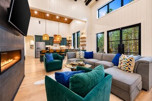 A spacious living area with a fireplace, a sofa set, and a dining area with chairs and a kitchen in the background. - Luxe & Kid Approved! Playset, EV, Meta VR Game (Broken Bow)
