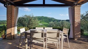 Eine überdachte Terrasse mit einer Ziegel-Säule, einem Tisch mit Stühlen und Blick auf eine grüne Landschaft.