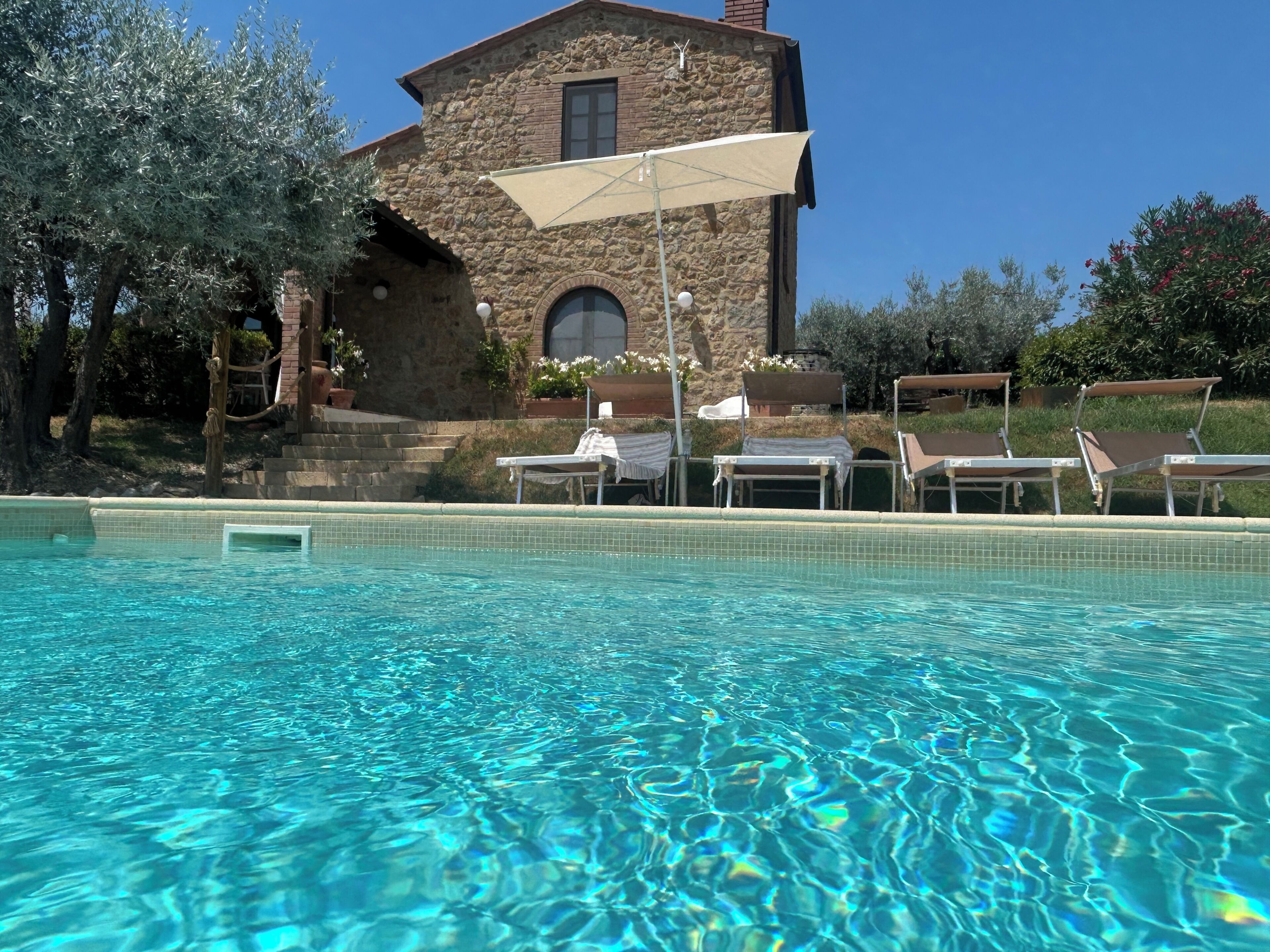 A swimming pool with clear water, surrounded by lounge chairs and a stone building with a window.