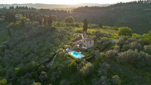 Luftaufnahme einer Villa mit Swimmingpool, umgeben von üppiger Vegetation und Hügeln.