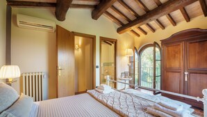 Ein Schlafzimmer mit einem großen Bett, Holzbalkendecke, einem Holzschrank, einem Fenster mit Blick und einer Heizung.