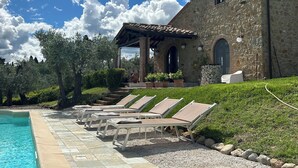 Ein Steinhaus mit Pool, Liegestühlen und einer Pergola.