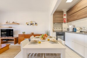 A modern kitchen with white cabinets, a dining table set with plates, glasses, and a fruit bowl. - #370 1BR Riamar | Sea View & Central (Armação de Pêra)