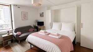 Ein Schlafzimmer mit einem Bett, einem Schreibtisch, einem Sessel, einer Couch und einem Fenster.