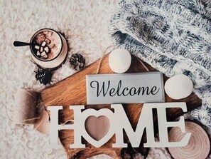 A cozy indoor setting with a 'Welcome HOME' sign, a wooden board, pine cones, and a bowl of what appears to be a hot beverage. - Bright studio in the heart of the Old Market (La Rochelle)