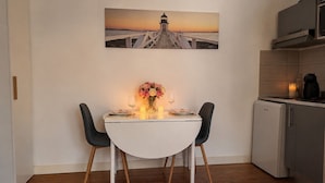 Ein Essbereich mit einem weißen Tisch, zwei Stühlen, einer Blumenvase und einem Gemälde eines Leuchtturms an der Wand.