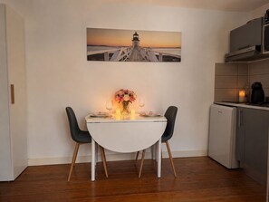 A dining area with a white table, two chairs, a vase with flowers, and a painting of a lighthouse on the wall. - Bright studio in the heart of the Old Market (La Rochelle)