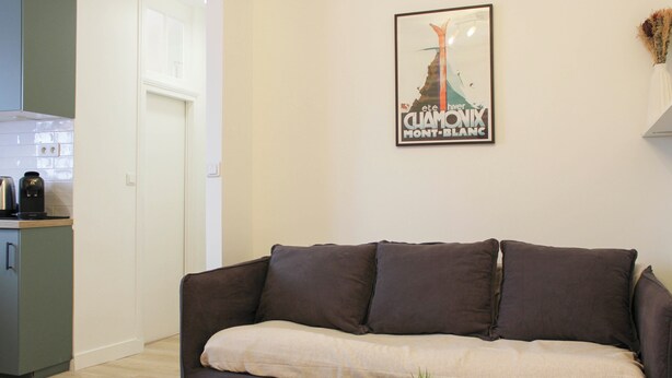 Ein Wohnzimmer mit einem dunkelbraunen Sofa, einem kleinen runden Tisch mit einer Pflanze und einem gerahmten Bild an der Wand.