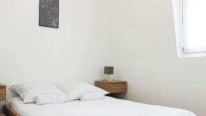 Ein Einzelbett mit weißer Bettwäsche, ein Holzkopfstück, ein Nachttisch mit Lampe und ein Wandbild.