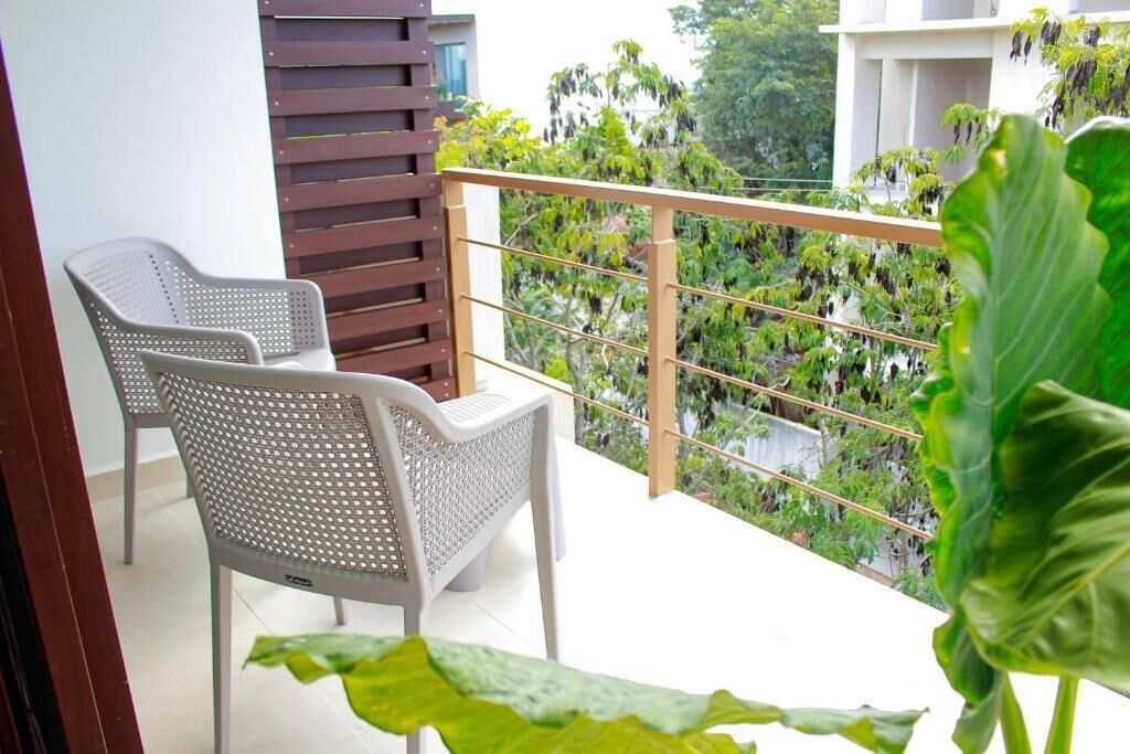 A balcony with two white chairs, a wooden slatted partition, and a view of green plants and trees.