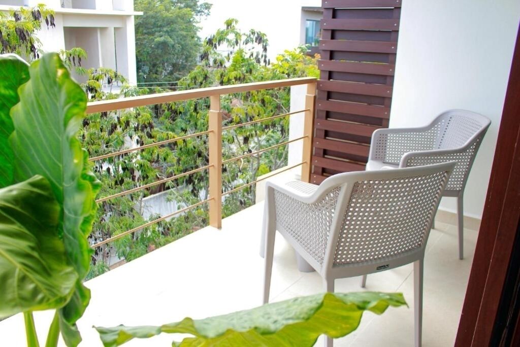 A balcony with two white plastic chairs, a wooden slatted partition, and a view of lush greenery.