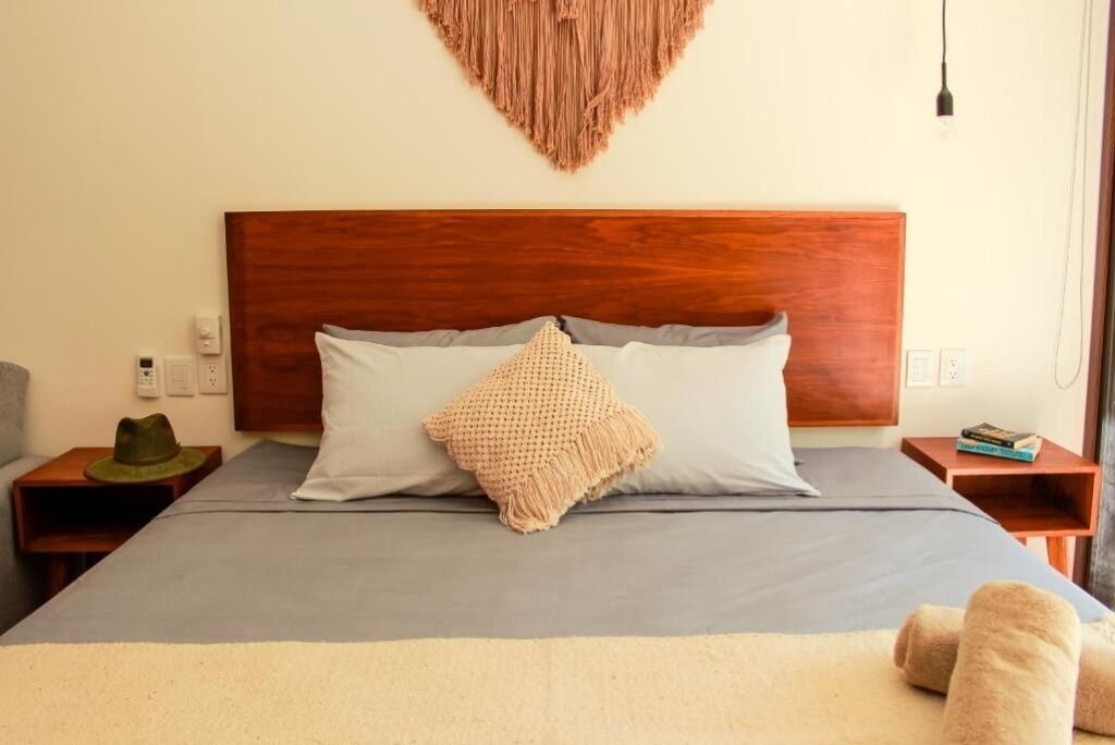 A neatly made bed with a wooden headboard, two pillows, a textured throw blanket, and a pair of towels on the floor.