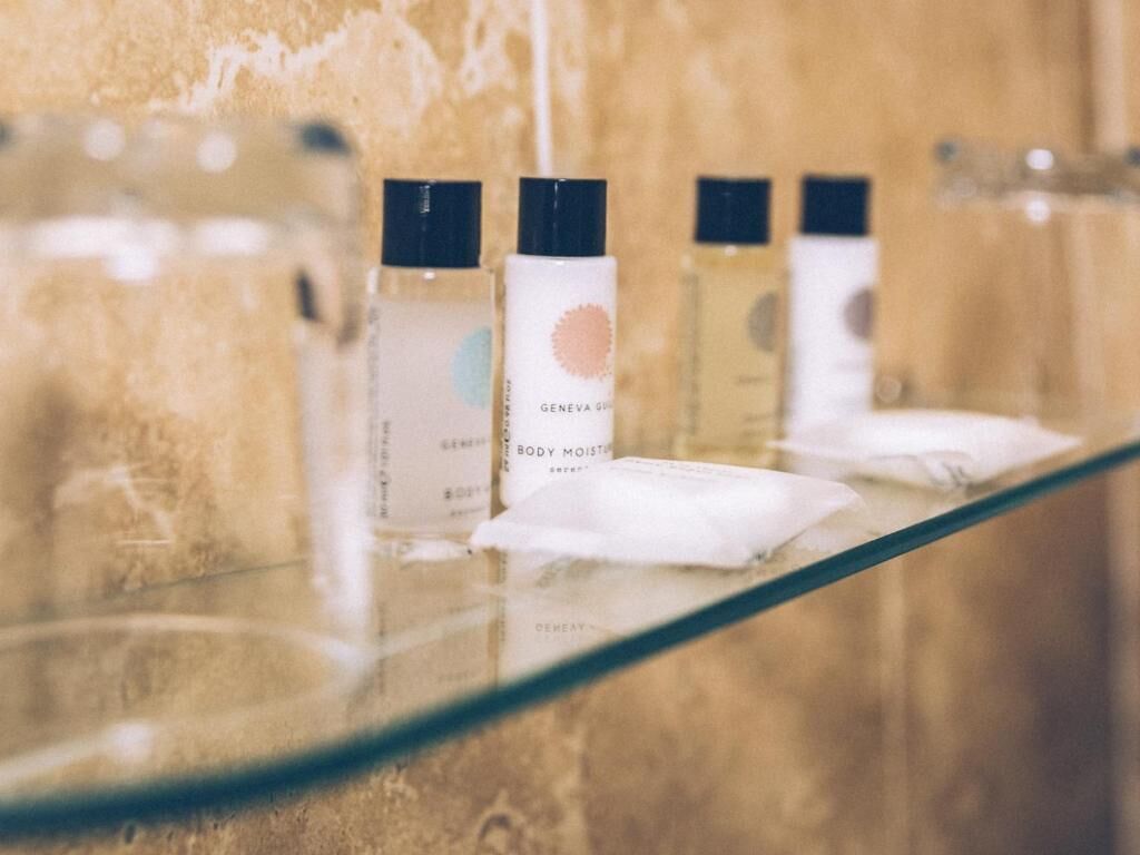 A glass shelf with three bottles of body mist and a tissue.