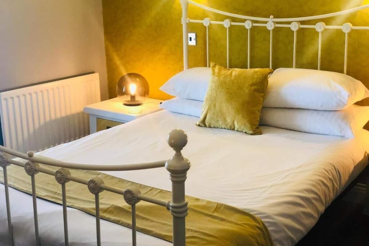 Ein Bett mit weißem Kopfteil, ein Nachttisch mit Lampe und eine Wand mit strukturierter Oberfläche.