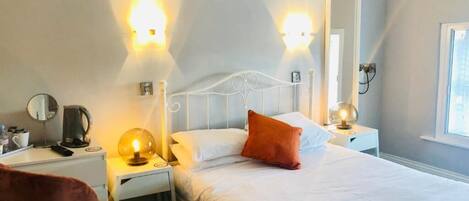 A hotel room with a bed, bedside tables, a chair, and wall-mounted lights.